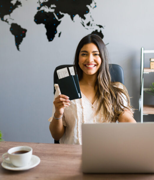 I am here to help you with your booking and travel questions. Female sales agent holding plane tickets while smiling and making eye contact at the travel agency